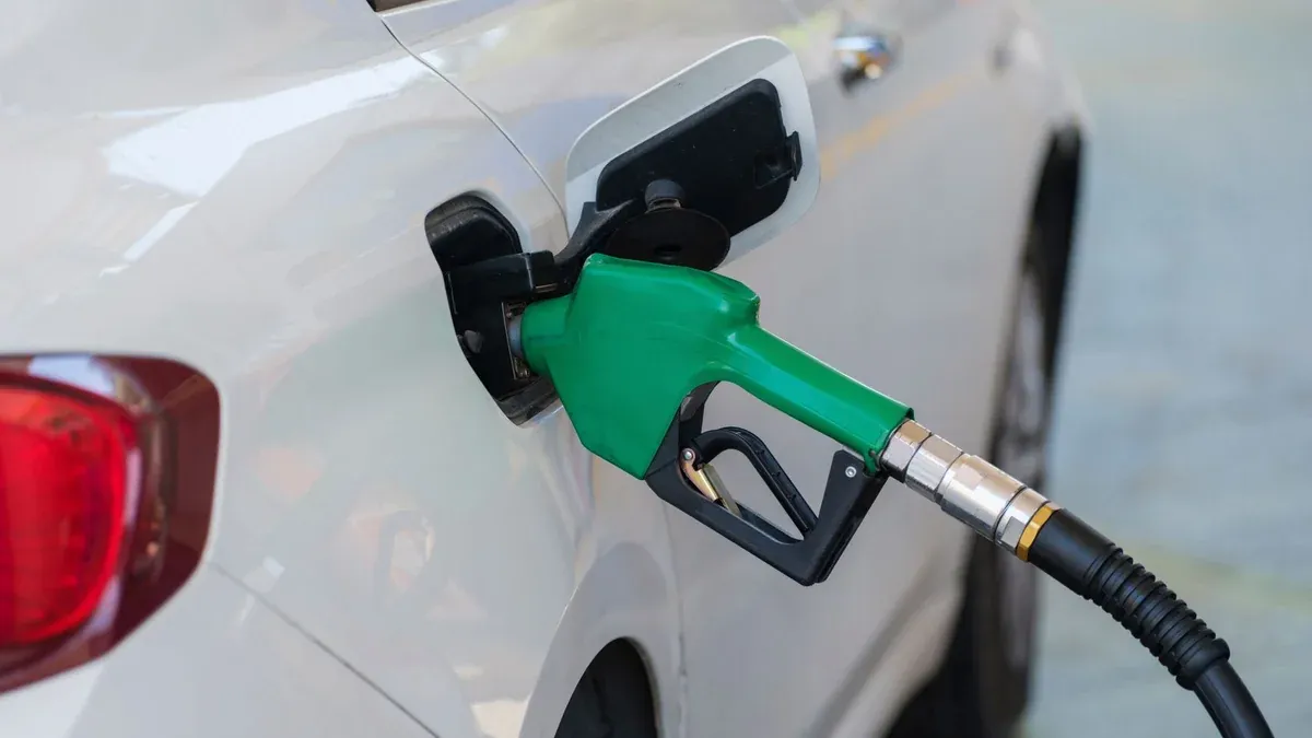 Close-up of a green nozzle refueling a white car at a gas station.