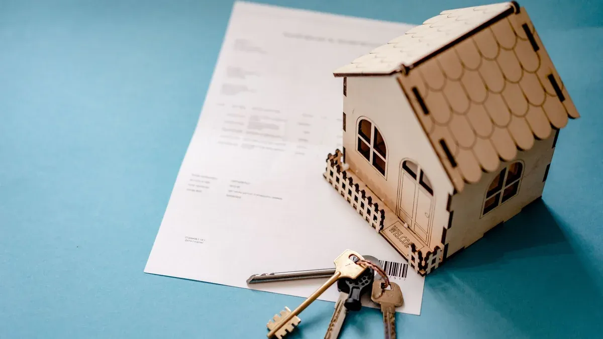 Miniature wooden house with keys and contract symbolizing real estate transactions.