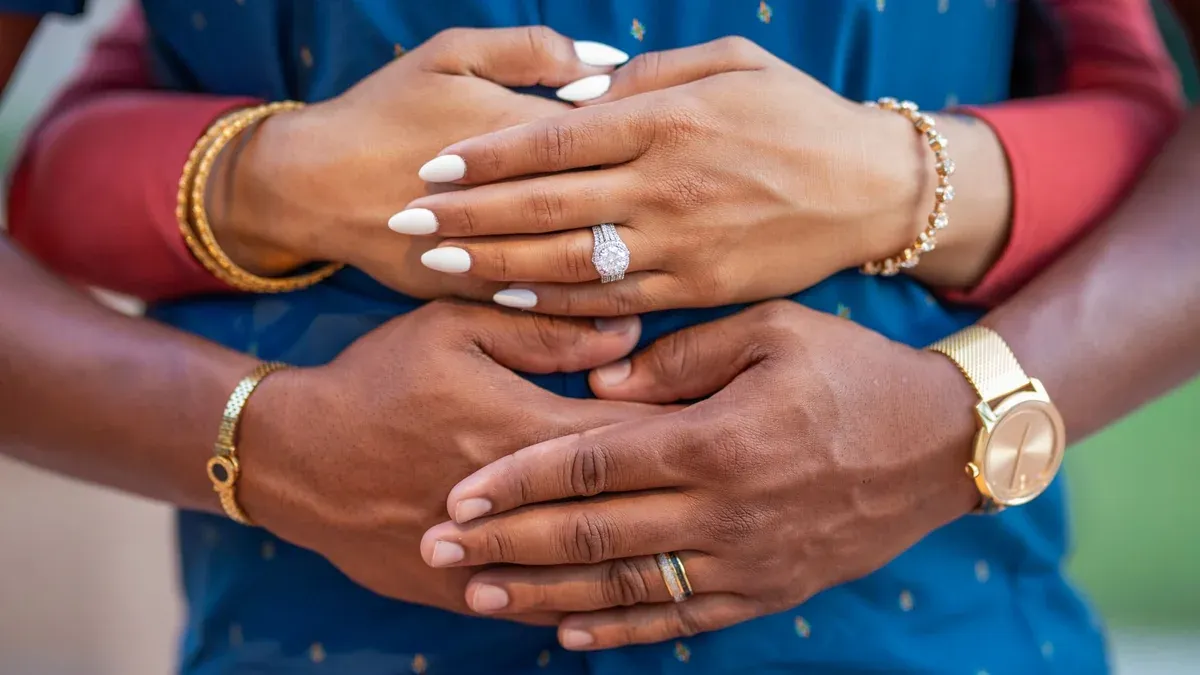 Intimate close-up shot of a couple's hands, showcasing elegant jewelry and engagement rings.