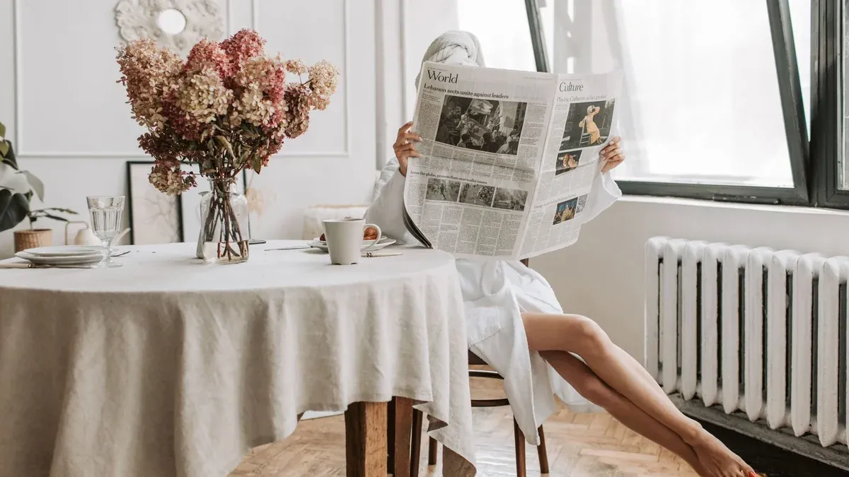 Woman enjoying a relaxing morning, reading a newspaper with coffee in a cozy setting.