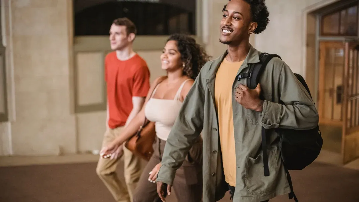 Positive African American man with male friend and Hispanic woman strolling in hallway of university building in campus on blurred background