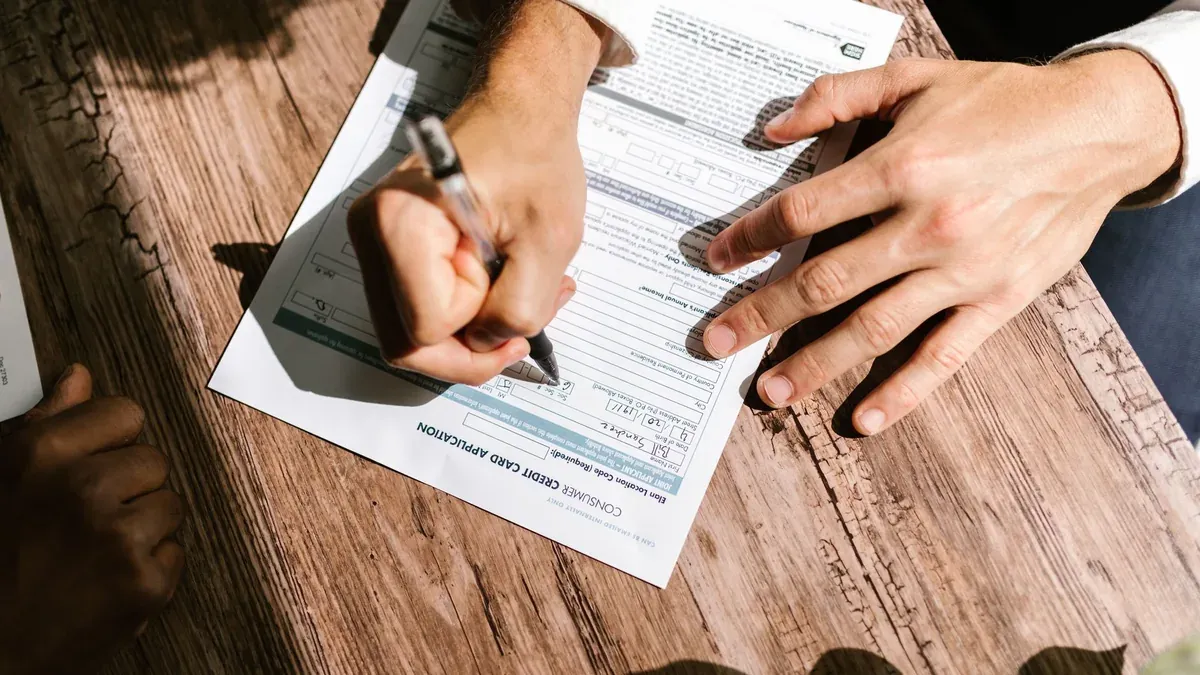 Hands writing on a consumer loan credit application form on a wooden table.