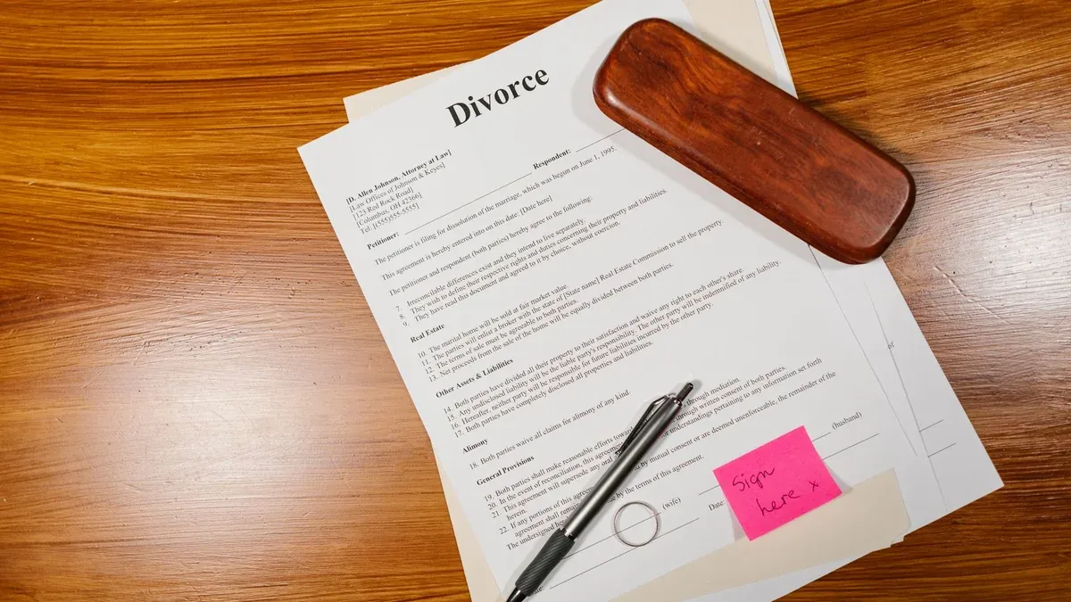 Flat lay of divorce papers with a pen and ring on a wooden table for legal themes.