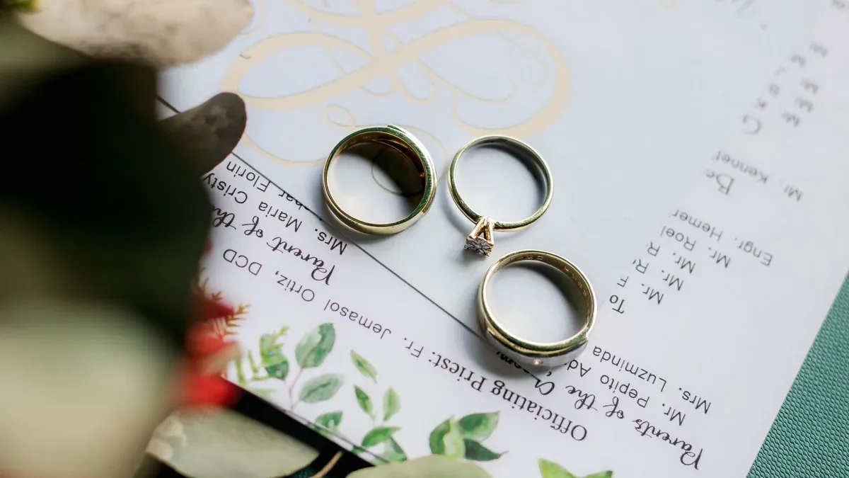From above of golden wedding rings placed on papers on table near bouquet of flowers in daytime