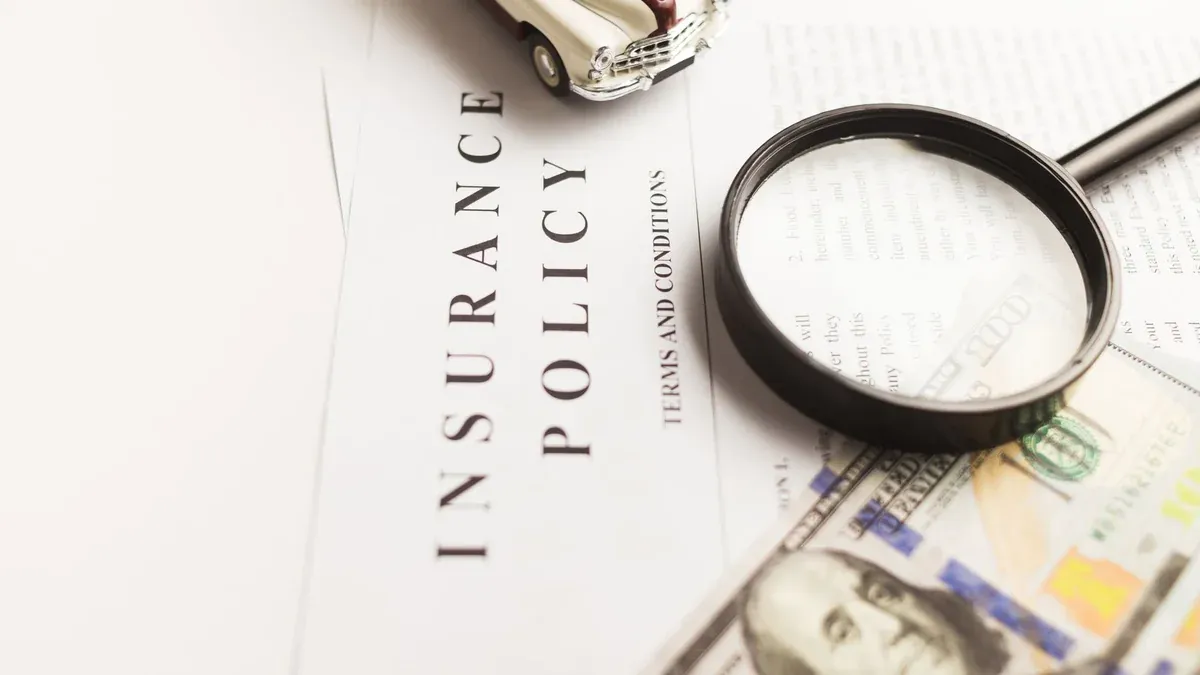 Close-up image of an insurance policy with a magnifying glass, money, and toy car.