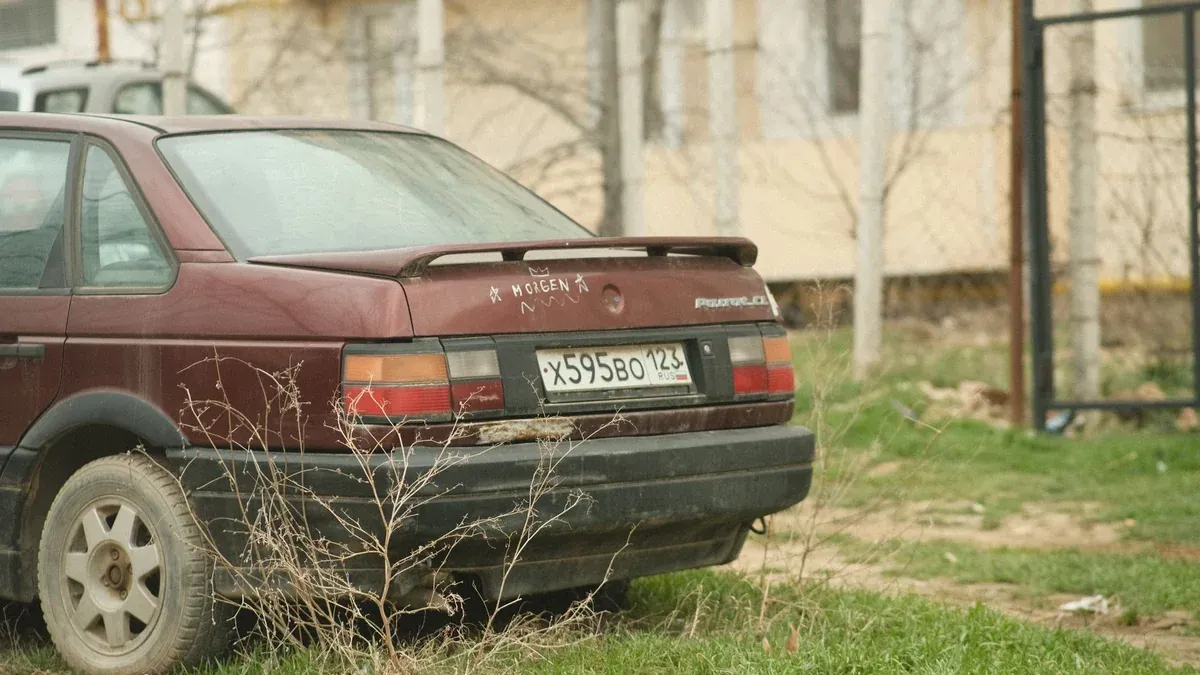 An old vintage car parked in a residential area with a focus on the trunk and license plate.