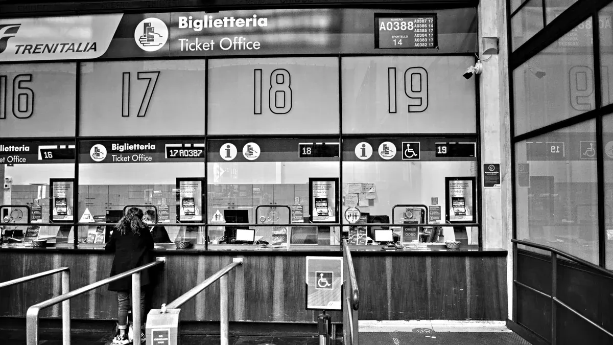 Monochrome image of a train station ticket office with numbered counters, showcasing travel services.