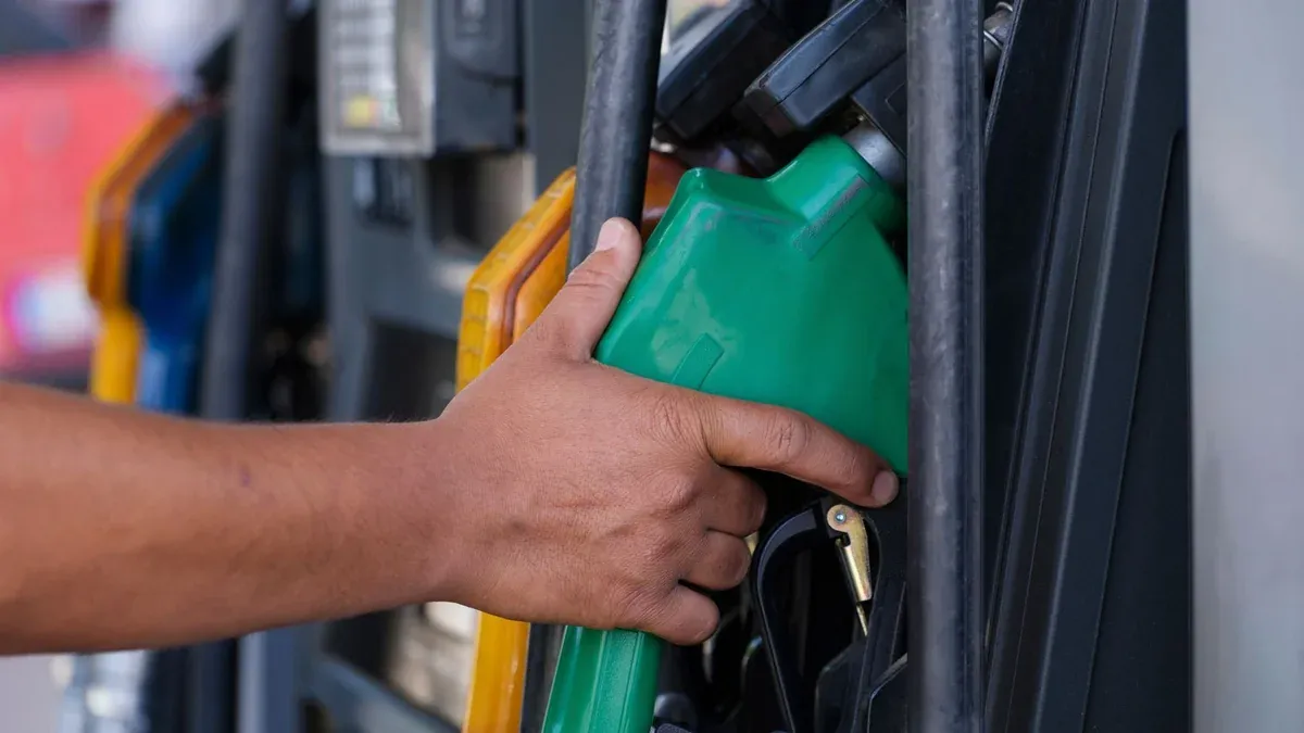Close-up of a hand holding a green fuel nozzle at a gas pump station outdoors.