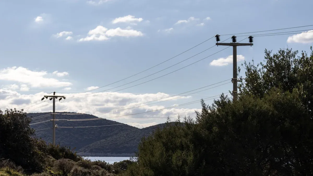 Electricity poles and power lines over scenic hills with a blue sky backdrop, symbolizing energy and nature.