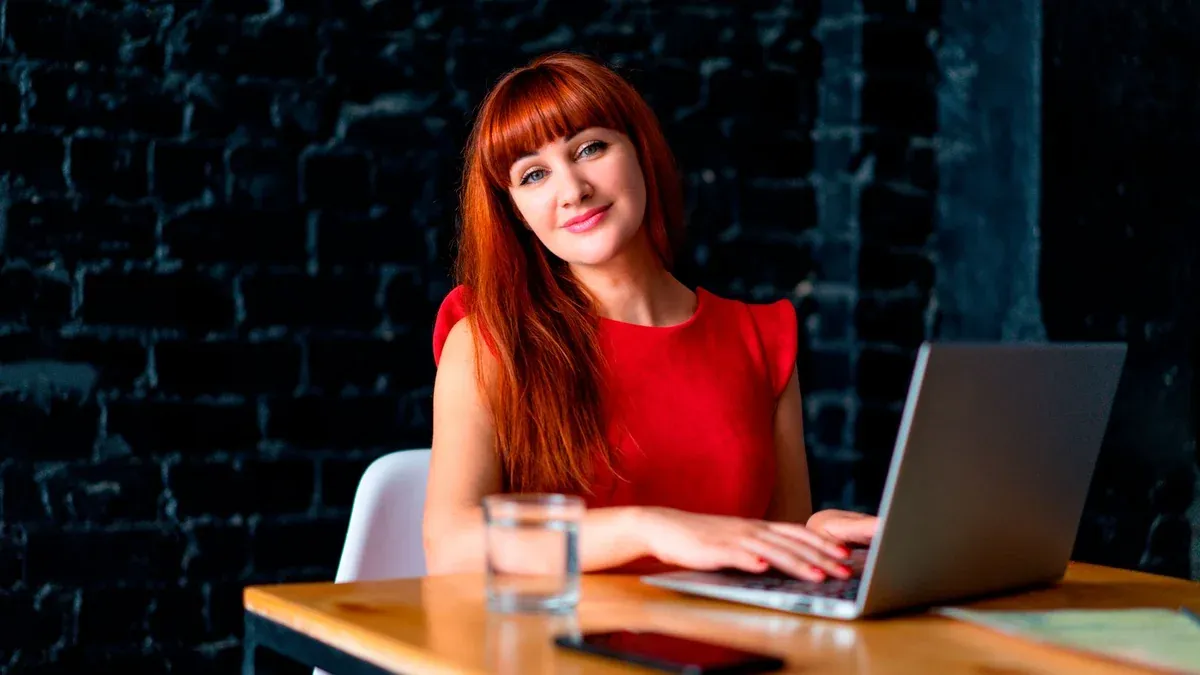 Redheaded woman in office working on a laptop, exuding professionalism and poise.