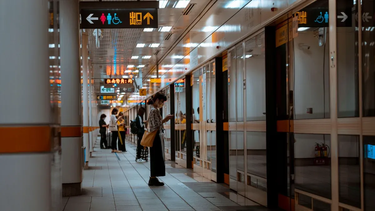 A bustling subway corridor with people standing and waiting near directional signs.