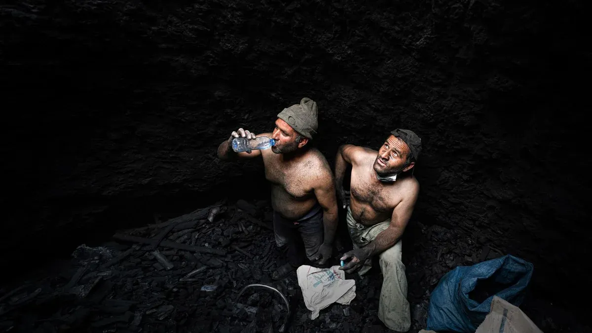 Two shirtless miners taking a break in a dark coal mine in Iran.