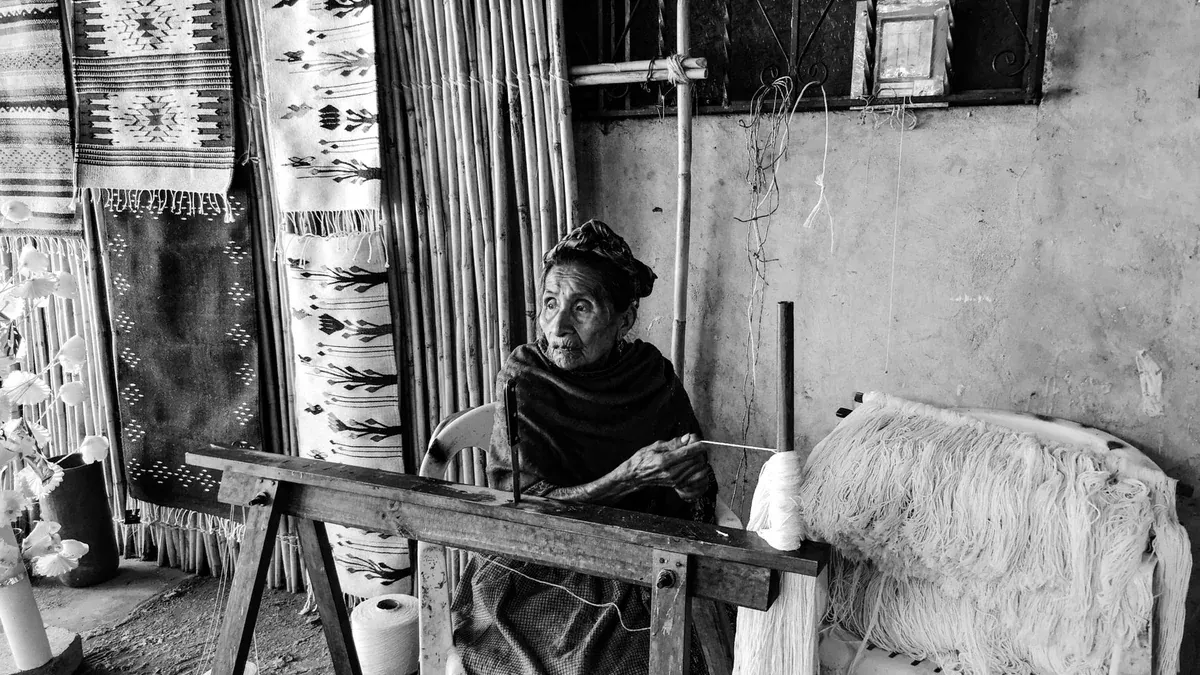 An elder artisan weaving carpets in a traditional workshop, Teotitlan del Valle, Mexico.
