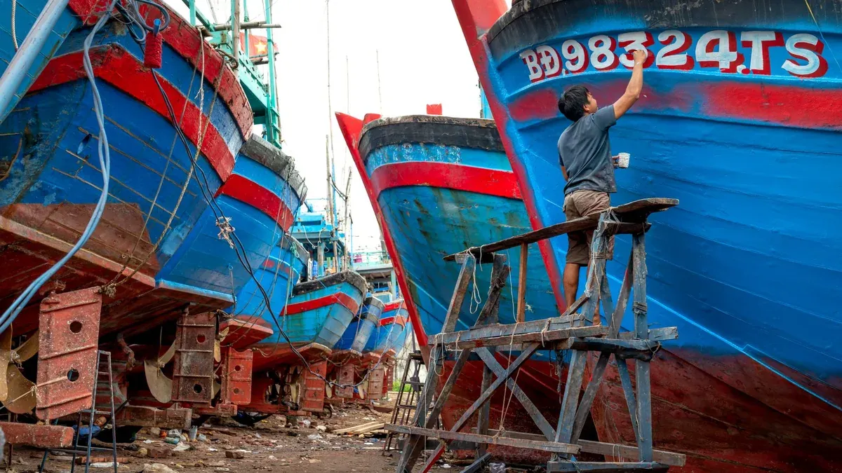 A man painting hulls of vibrant boats in an outdoor shipyard.