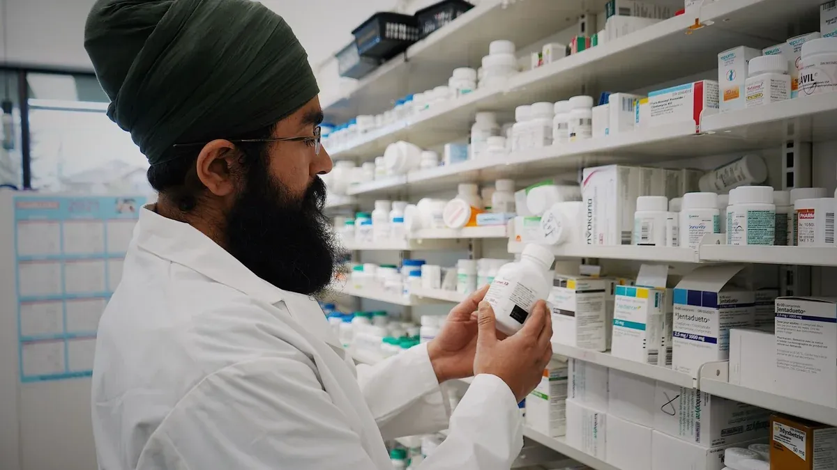 Pharmacist with turban organizing shelves in a pharmacy, focused on healthcare.
