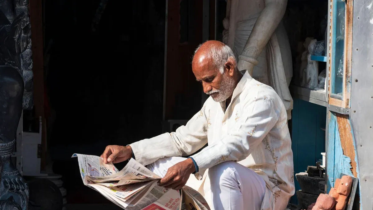 Elderly man in traditional attire reading a newspaper outside in Jaipur, India.