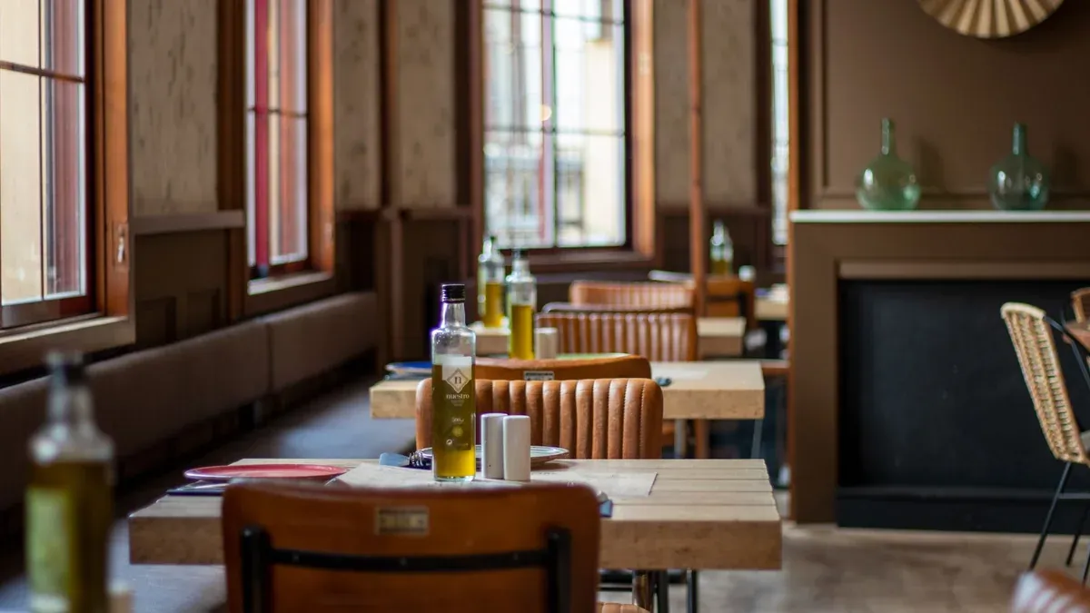 Inviting restaurant interior featuring wooden tables with olive oil bottles and leather chairs in focus.