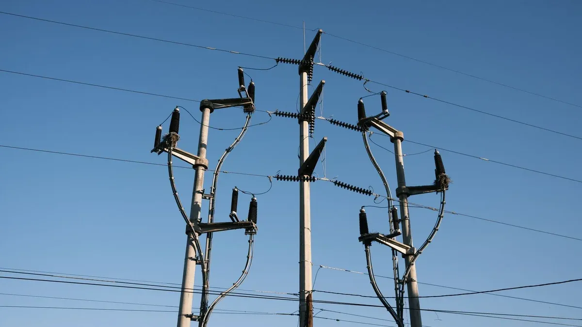 High-voltage power lines and poles silhouetted against a clear blue sky, representing energy distribution.