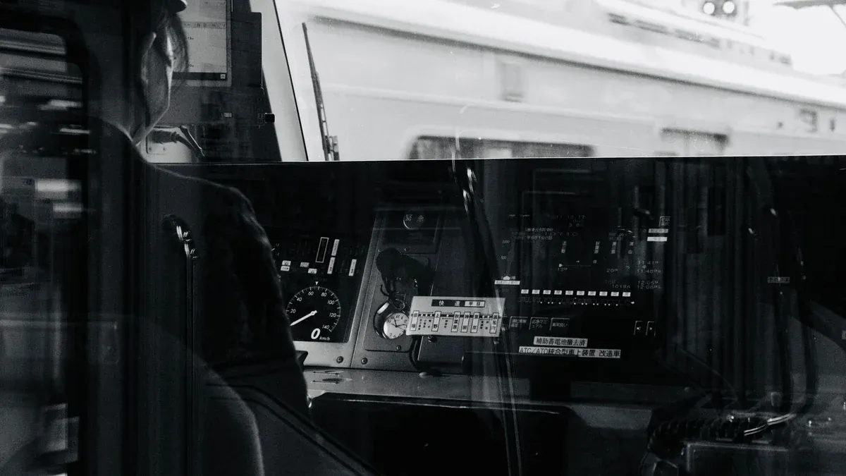 Monochrome image of a train driver's cockpit showing controls and reflections.