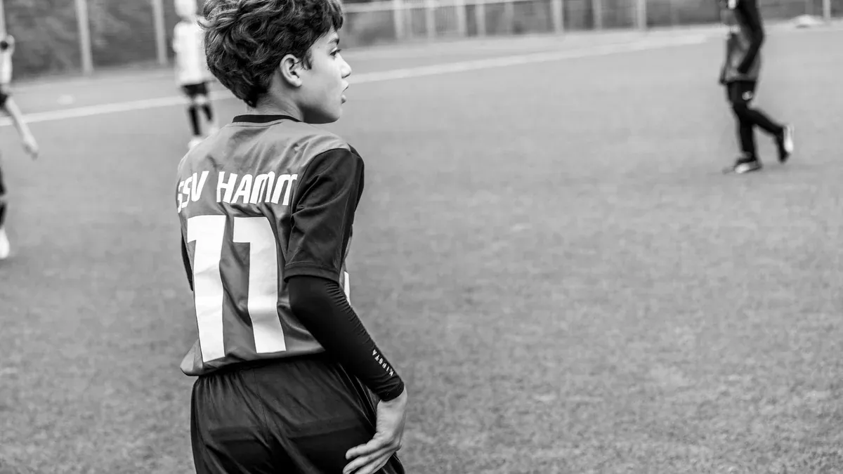 A young soccer player on a football pitch wearing a team jersey in Germany.