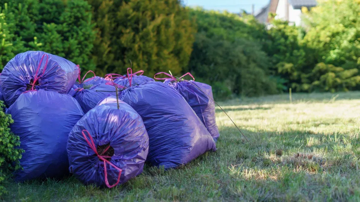 Vibrant purple trash bags stacked in a sunlit garden setting, ideal for spring clean-up visuals.