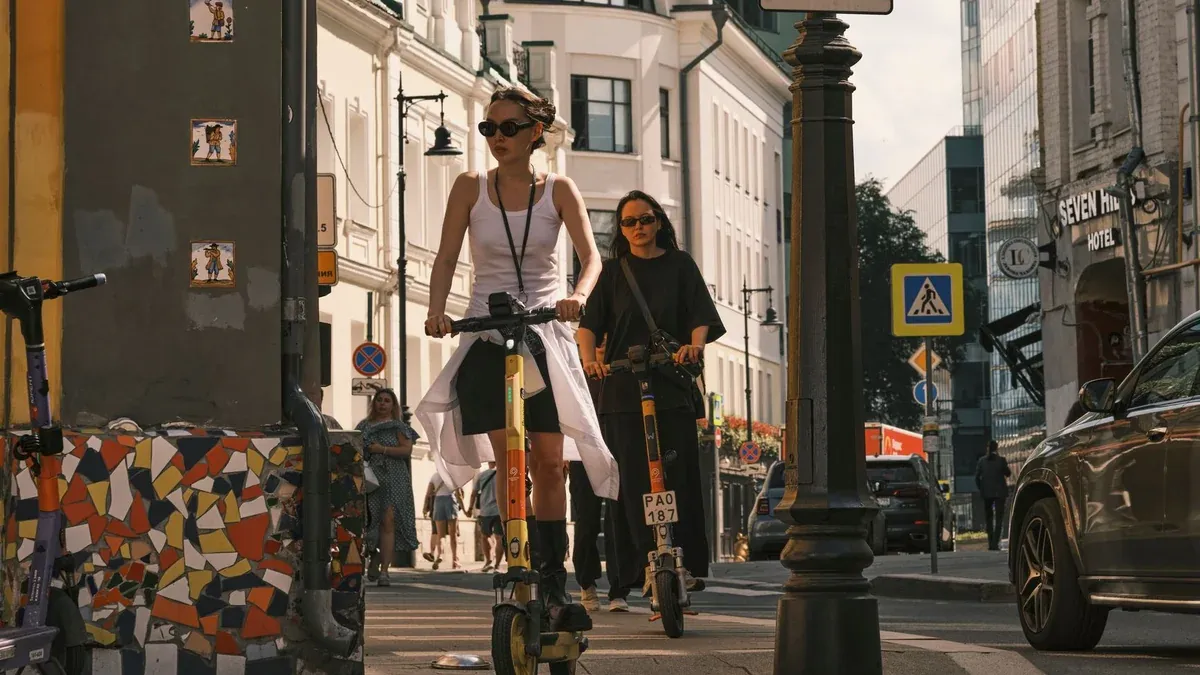 Two women riding electric scooters on a city street, showcasing urban commute.