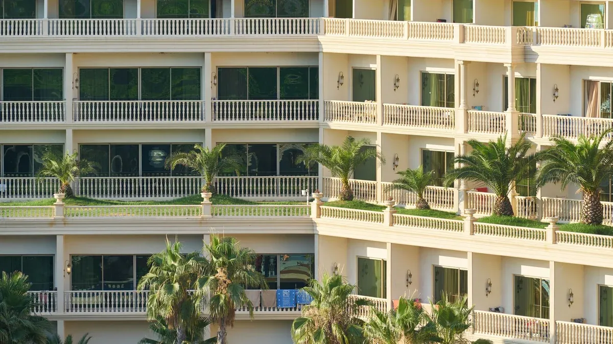Elegant apartment building exterior with lush palm trees and balconies, ideal for vacation living.