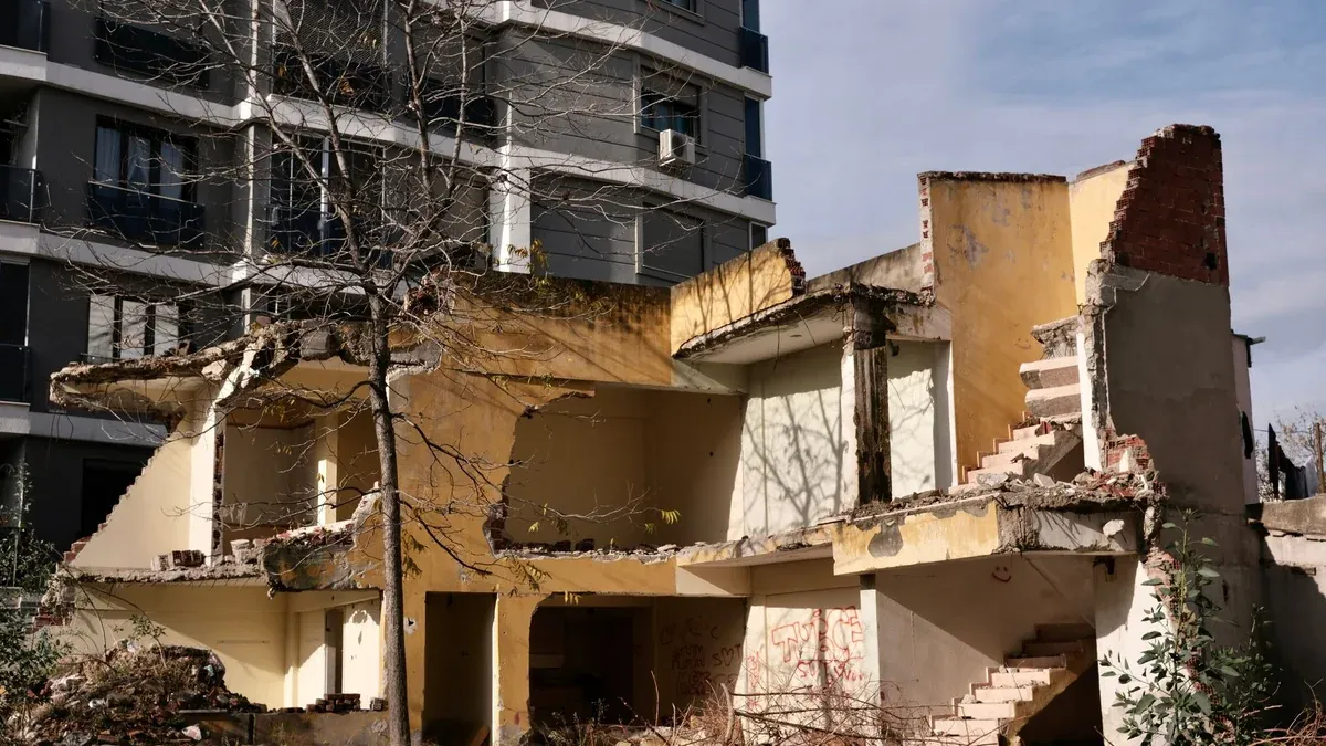 A dilapidated two-story building in İzmir set against a modern apartment backdrop.