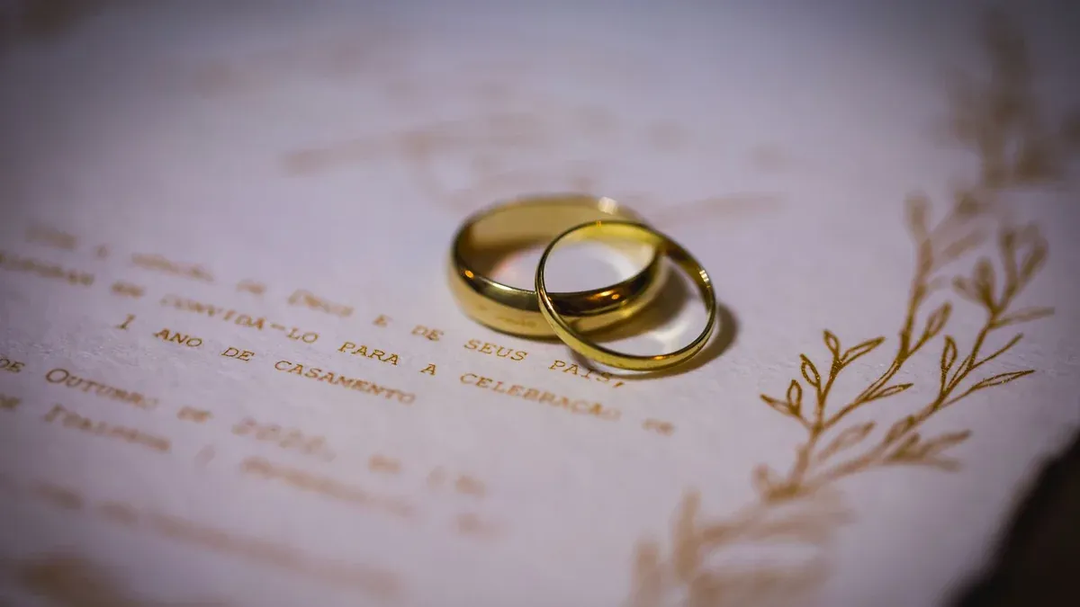 Close-up of gold wedding rings on a white wedding invitation with elegant floral design.