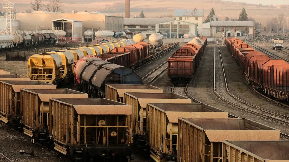 A busy freight train yard with multiple tracks and a variety of train cars in a rural setting.