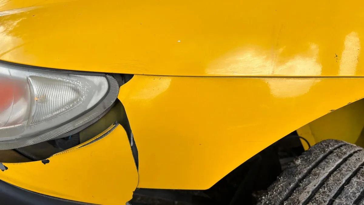 Close-up image of a yellow car's damaged front bumper and headlight for insurance or accident concept.