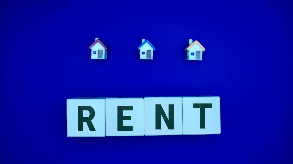 Miniature houses above letters spelling 'RENT' on a blue background, ideal for real estate themes.