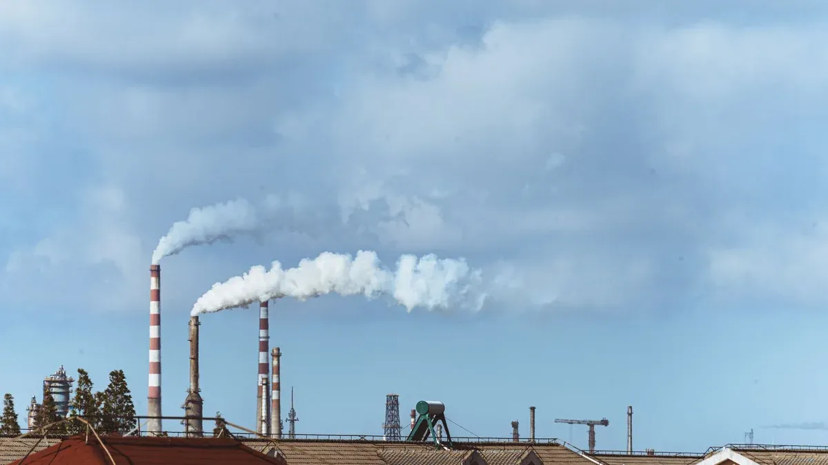 Factory chimneys emitting smoke over rooftops on a clear day, illustrating urban pollution.
