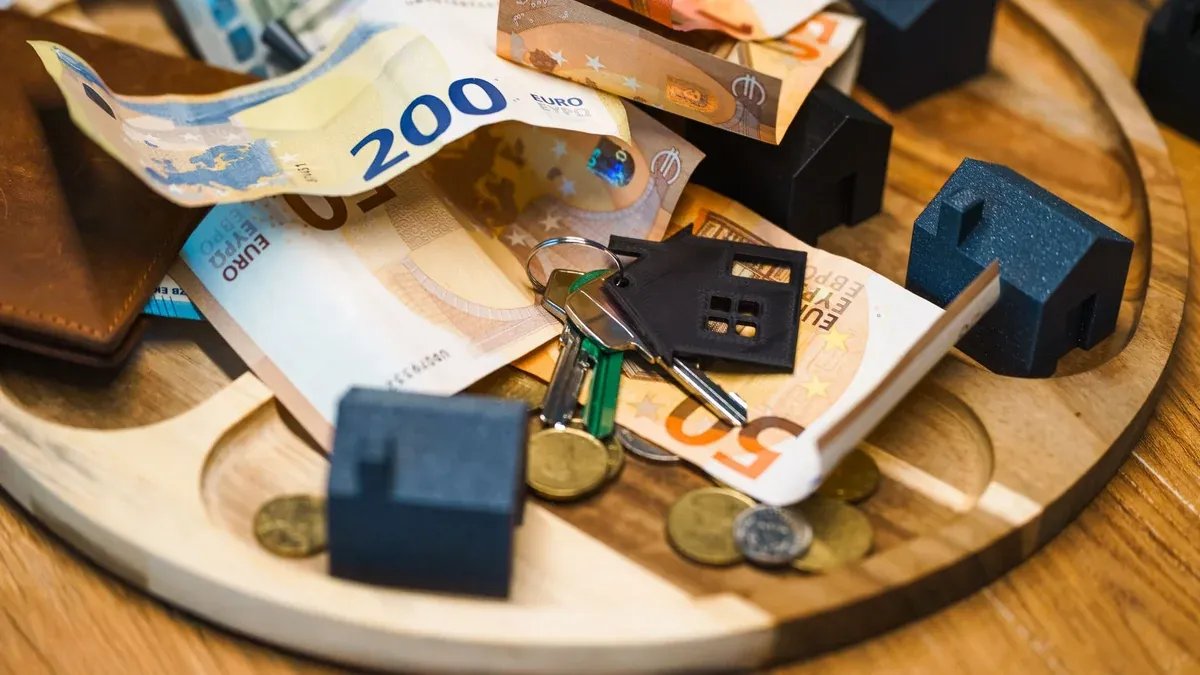 Euro currency, keys, and miniature houses symbolize real estate and finance concepts.