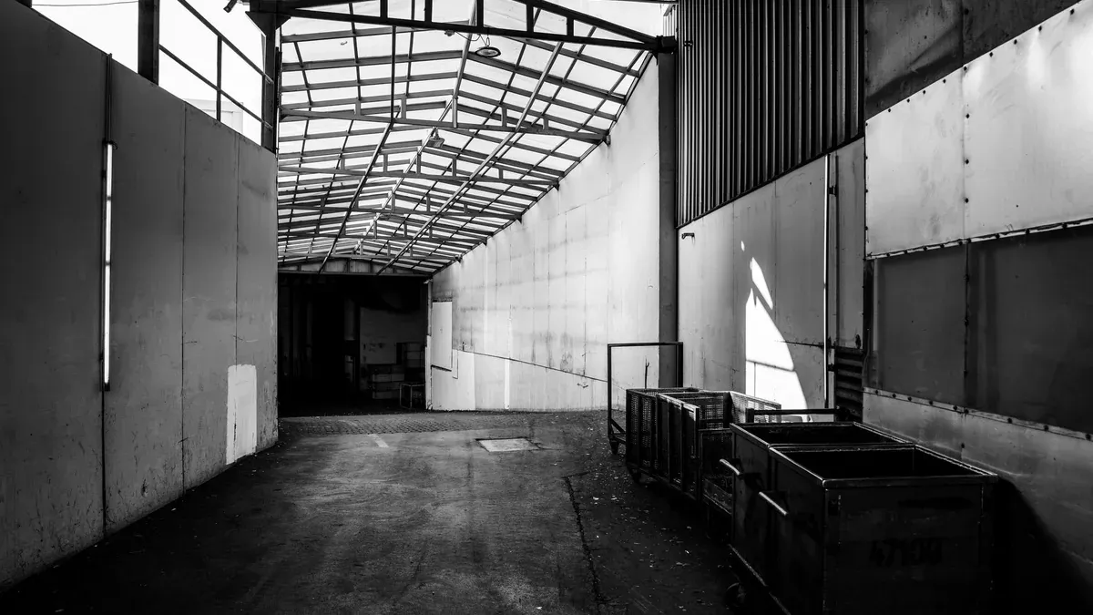 Black and white photo of an empty industrial warehouse corridor with metal containers.