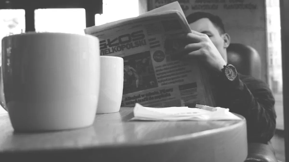 Adult man enjoying a relaxing moment in a café, reading a newspaper with a cup of coffee nearby.