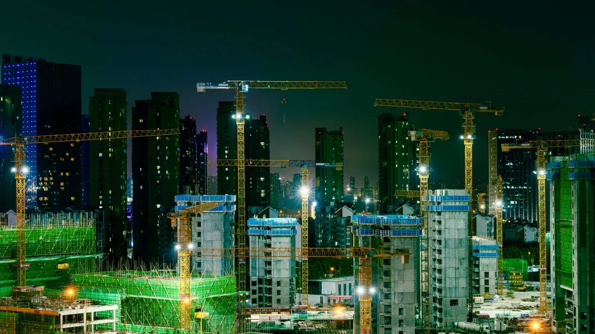 Night view of a bustling construction site in an urban cityscape with cranes and high-rise buildings.