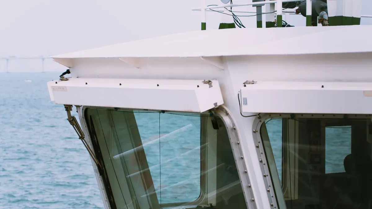 Close-up of a ship's bridge with ocean view and partial skyline in the background.