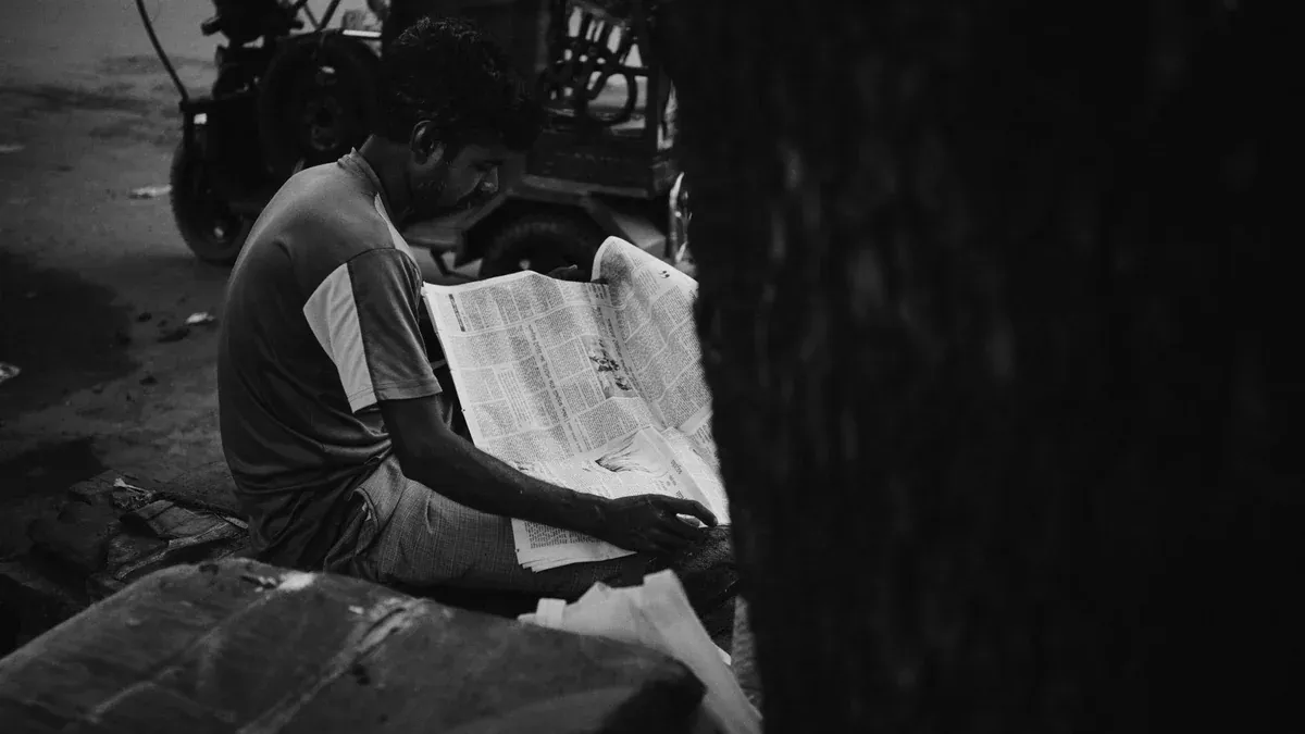 A man engrossed in reading a newspaper on a quiet morning street in Kurigram, Bangladesh.