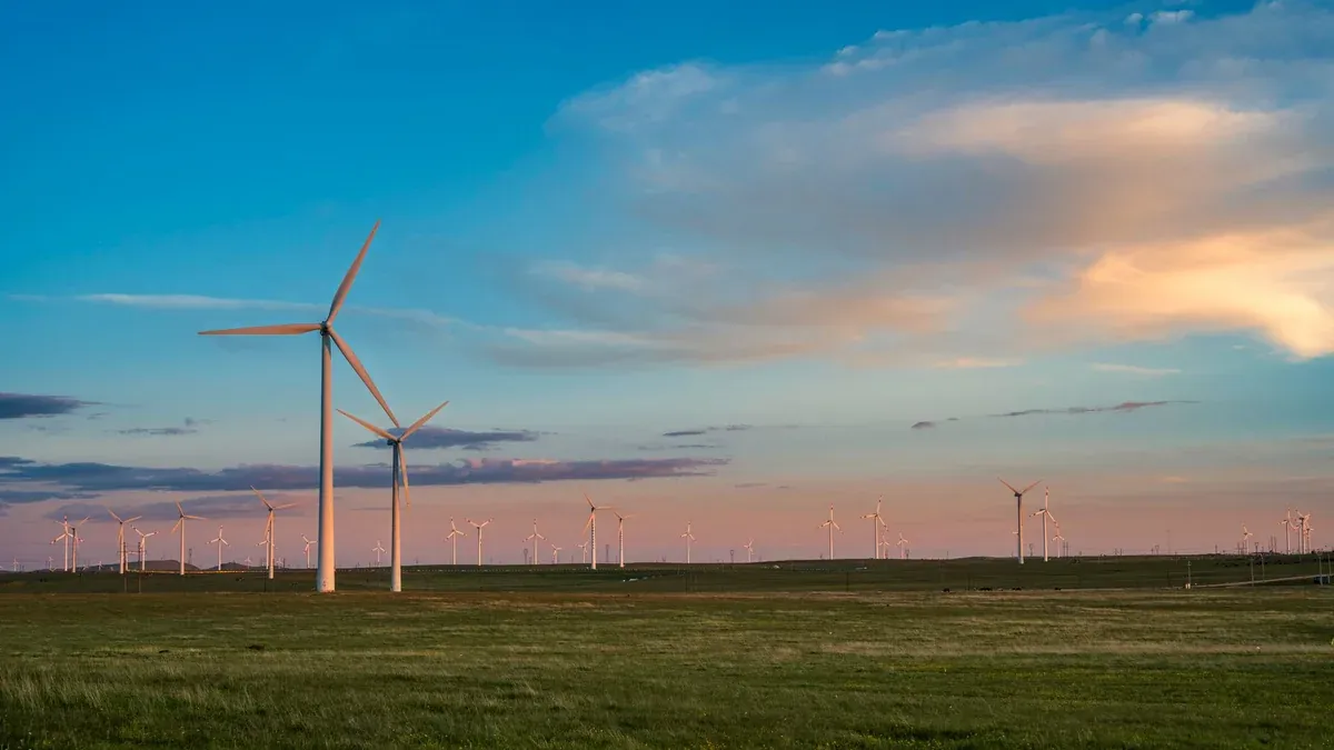 View of a wind farm with multiple turbines under a colorful dusk sky. Renewable energy source.