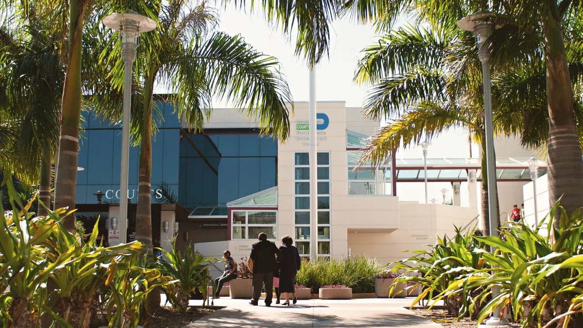 Miami courthouse with palm trees and people under a bright sky, showcasing a tropical setting.