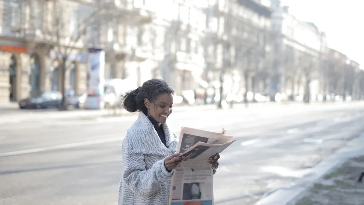 African American woman reading a newspaper on an urban street, enjoying a peaceful morning.