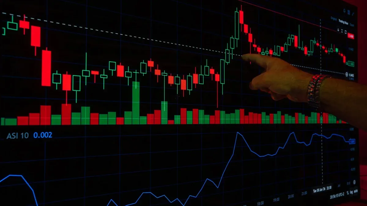 A hand points at a stock market graph on a digital screen, highlighting financial trading trends.