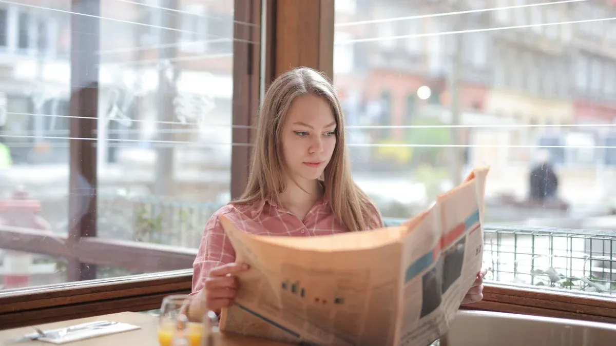 A young woman enjoying a newspaper at a cafe table, immersed in reading.