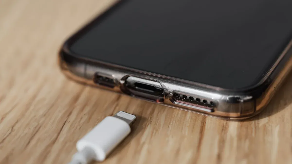 Modern cellphone in transparent cover with closeup of charging input and mobile phone white charger cable usb connector on wooden table
