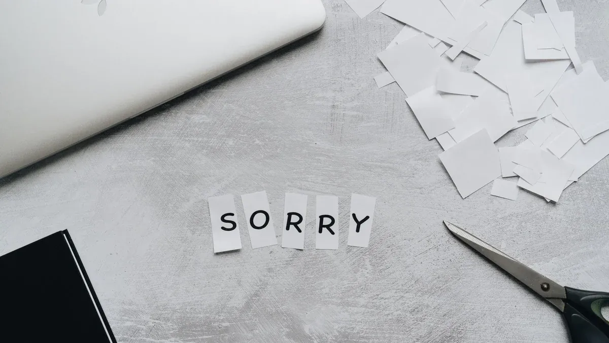 Top view of a desk with cut-out letters spelling 'sorry', scissors, and a laptop.