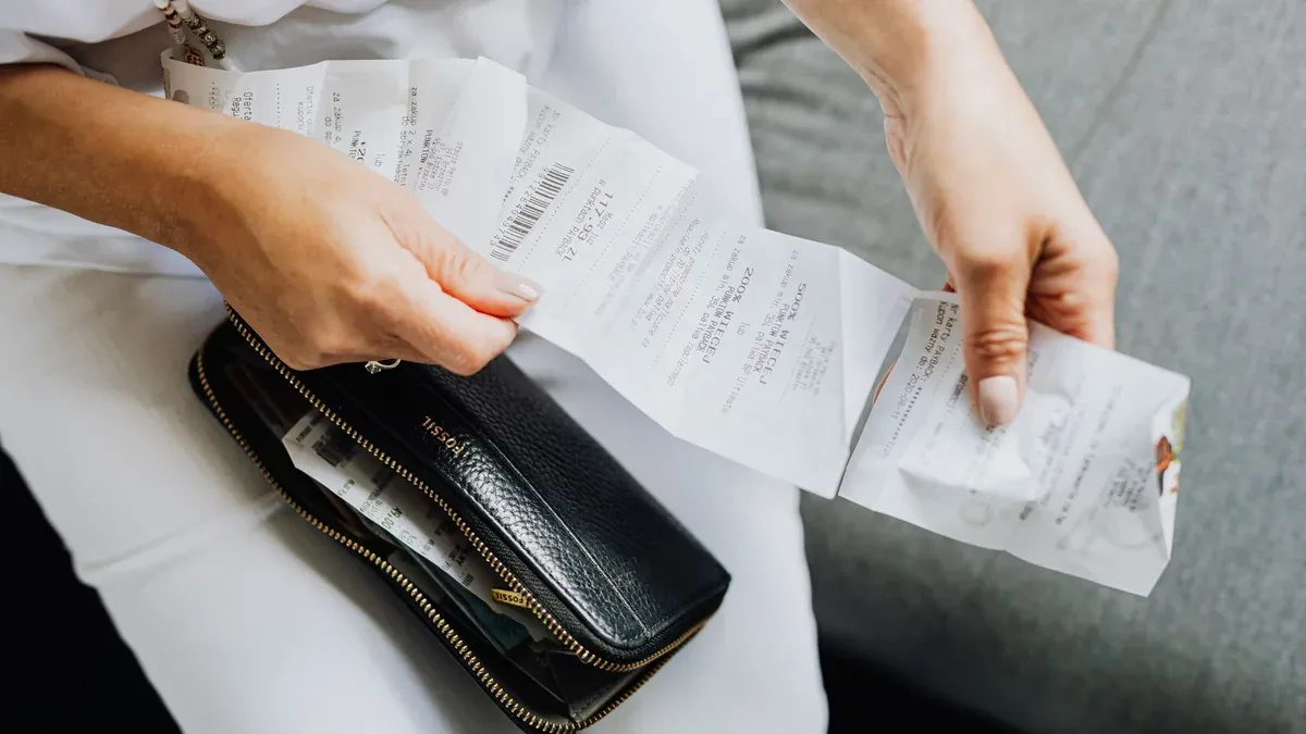 Close-up of a woman's hands managing multiple receipts taken from a black wallet.
