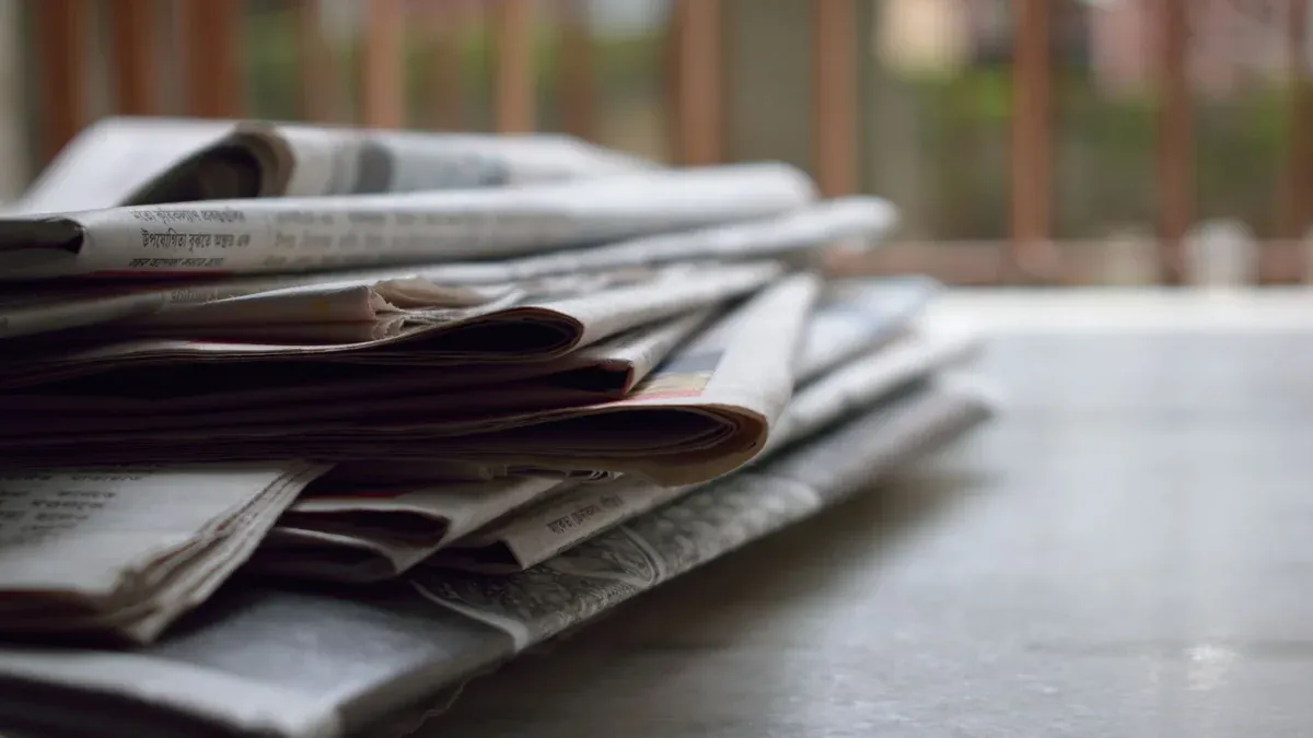 A close-up of a stack of newspapers resting on a desk, symbolizing information and media.