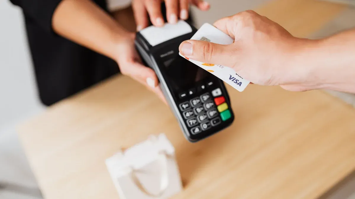 Close-up of hands using a contactless payment terminal with a credit card indoors.