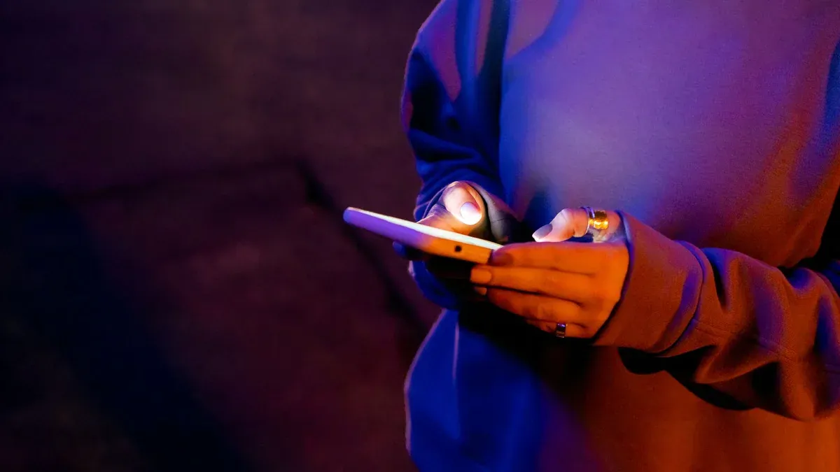 A person in a sweatshirt using a smartphone at night illuminated by screen light.